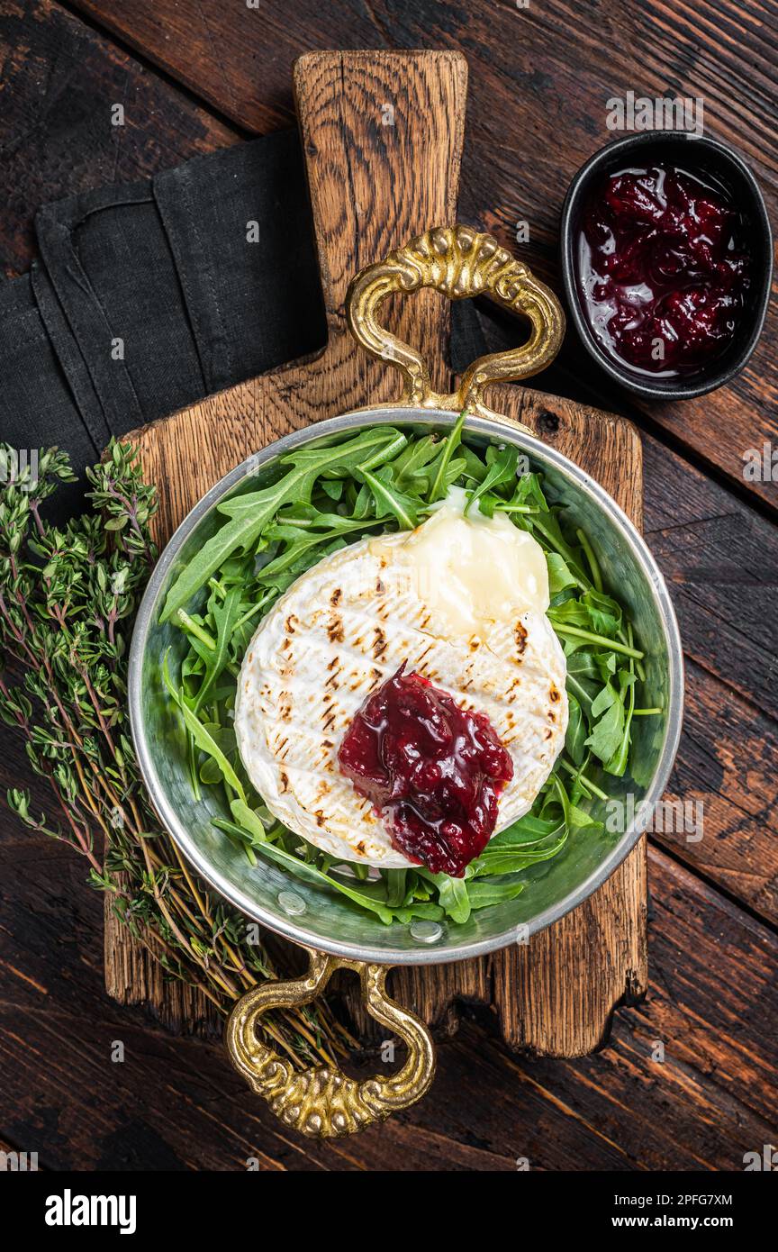 Baked Camembert Brie cheese with a cranberry sauce and garnished with arugula salad in a skillet