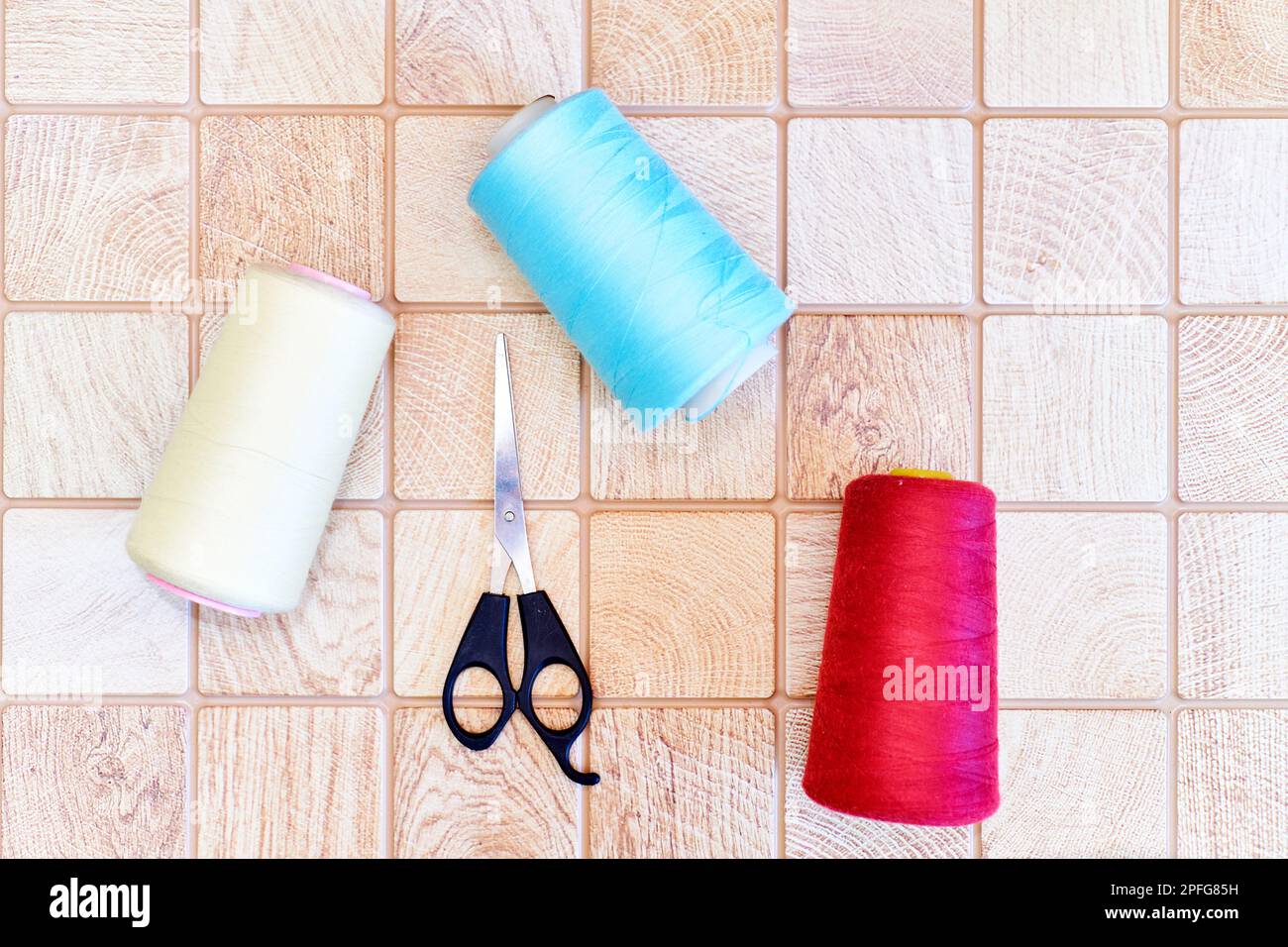 Multi colored threads and tailor scissors on a wooden plaid surface Stock Photo