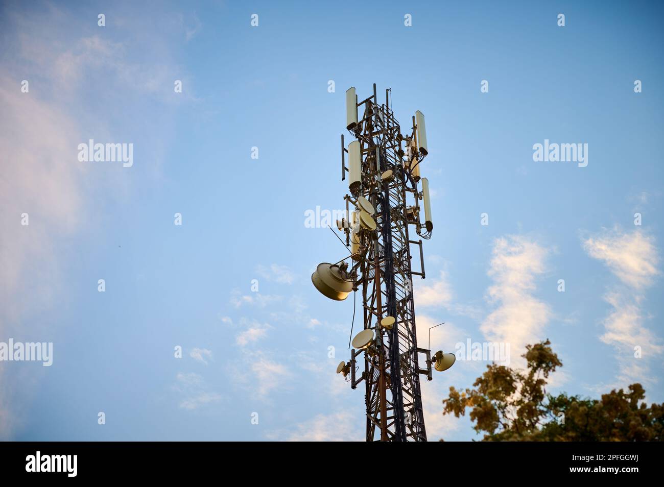 5G transmitter mast against the blue sky between the trees Stock Photo