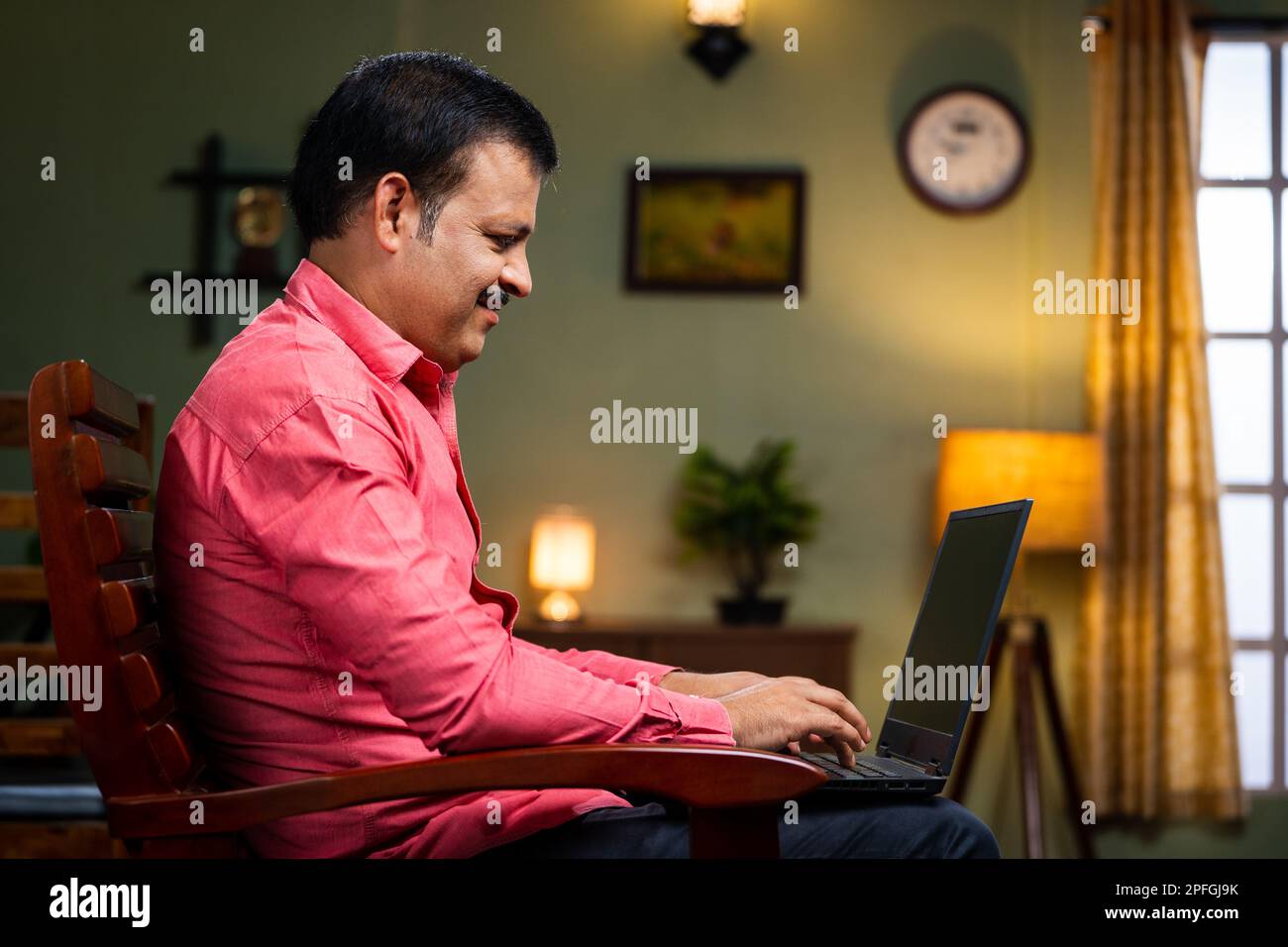 Middle aged man busy working on laptop on chair at home - concept of technology, entrepreneur and surfing internet. Stock Photo