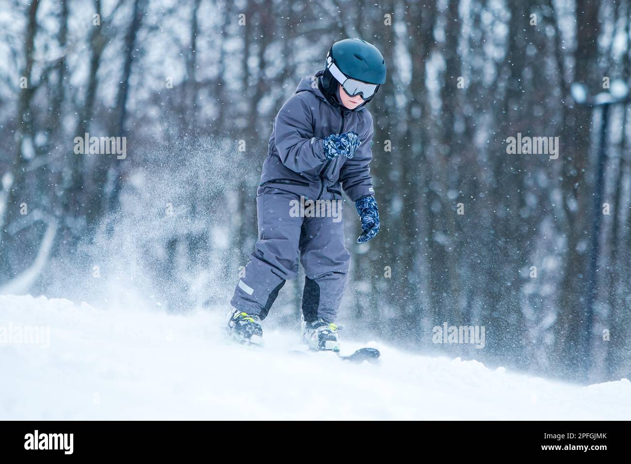 Little skier riding downhill with snow splash. Child skiing in mountains. Active teenage boy with safety helmet, goggles and ski poles running down Stock Photo