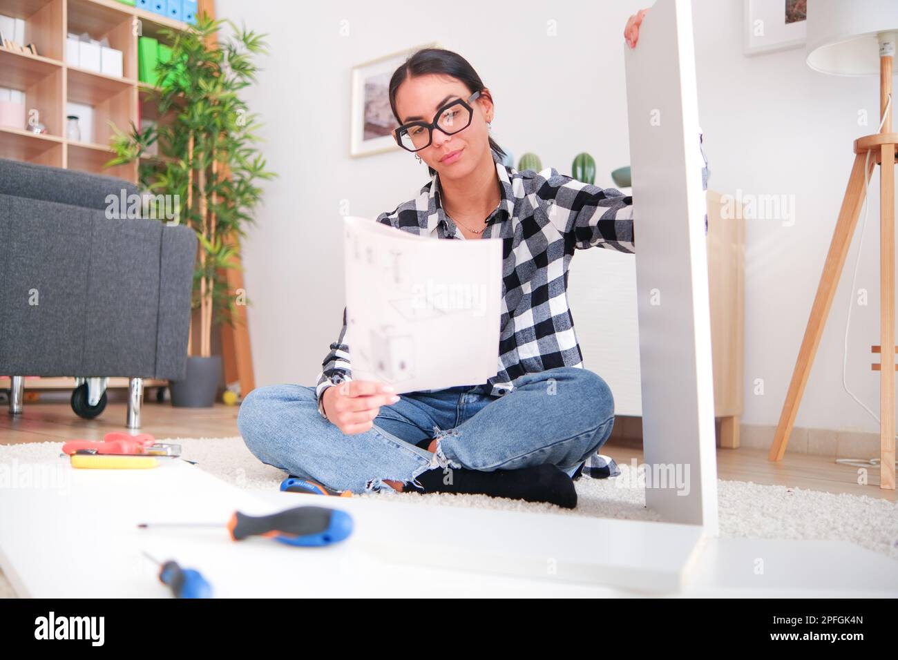 Woman who is assembling furniture in her home as part of a renovation project. She is using a variety of tools Stock Photo