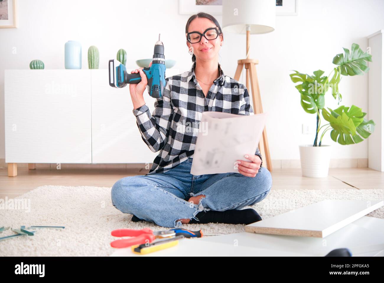 Woman who is assembling furniture in her home as part of a renovation project. She is using a variety of tools Stock Photo