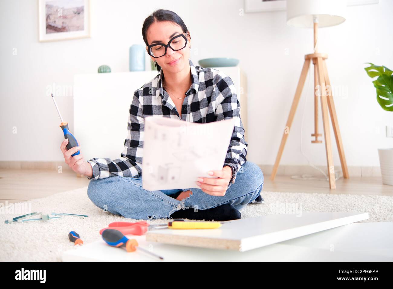 Woman who is assembling furniture in her home as part of a renovation project. She is using a variety of tools Stock Photo