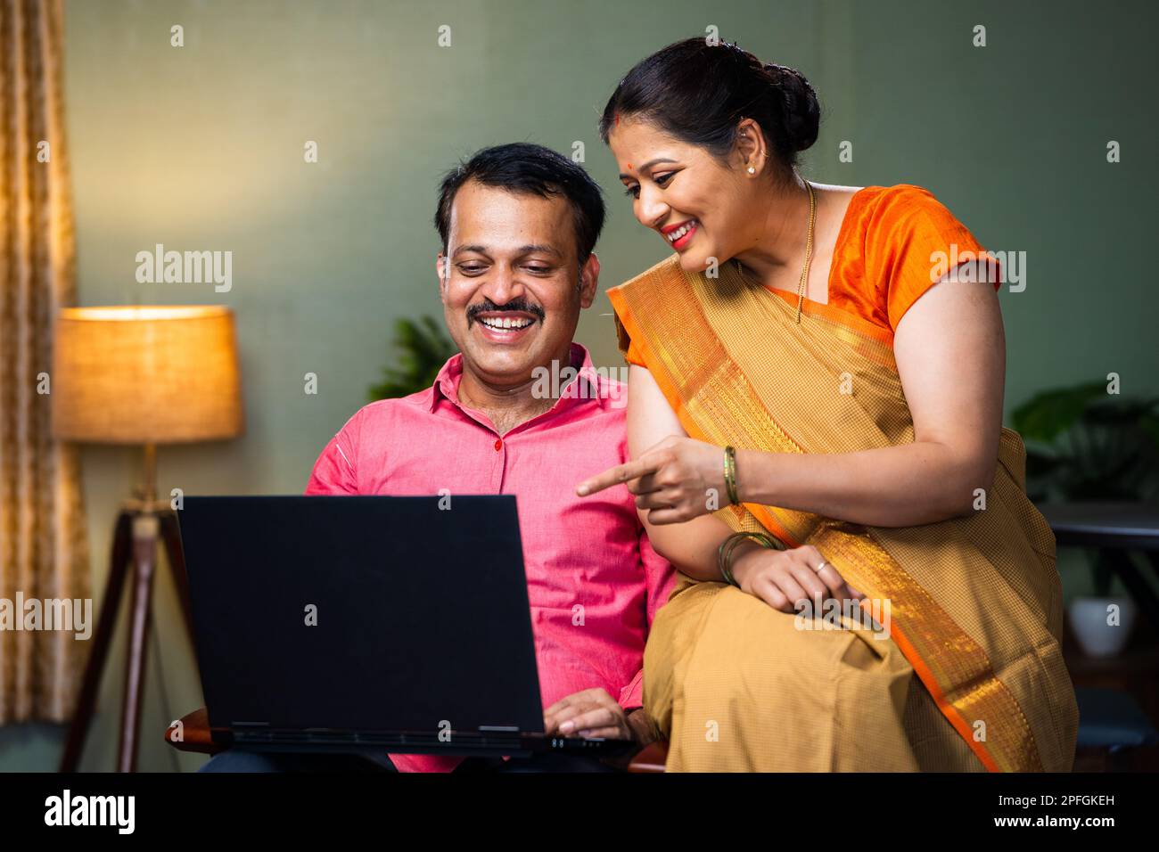 Happy smiling couple discuissing from laptop while sitting on chair at home - concept of relationship bonding, technology and online shopping Stock Photo