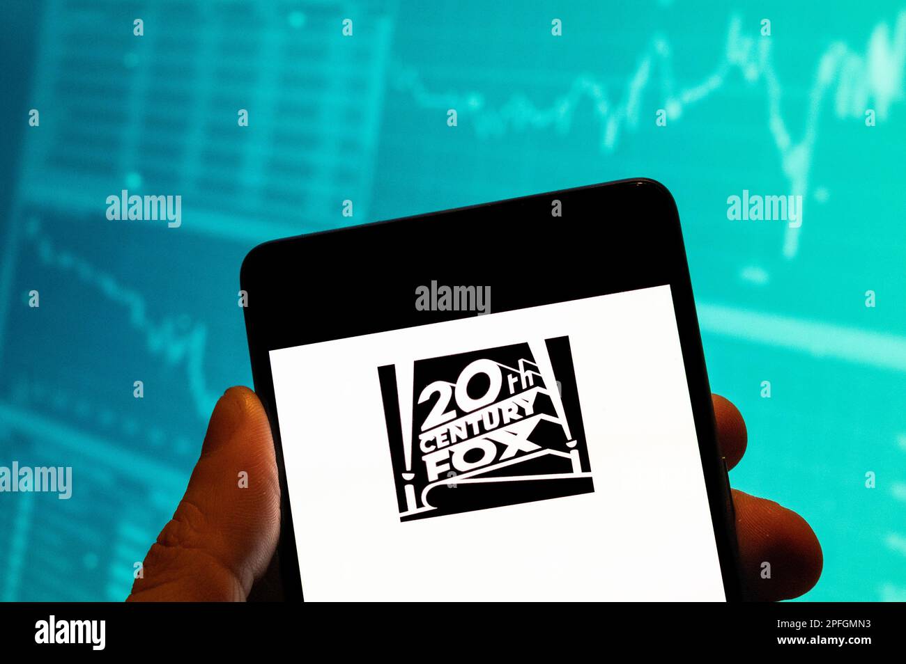 In this photo illustration, the American film studio Twentieth 20th Century Fox Film Corporation logo is seen displayed on a smartphone with an economic stock exchange index graph in the background. Stock Photo