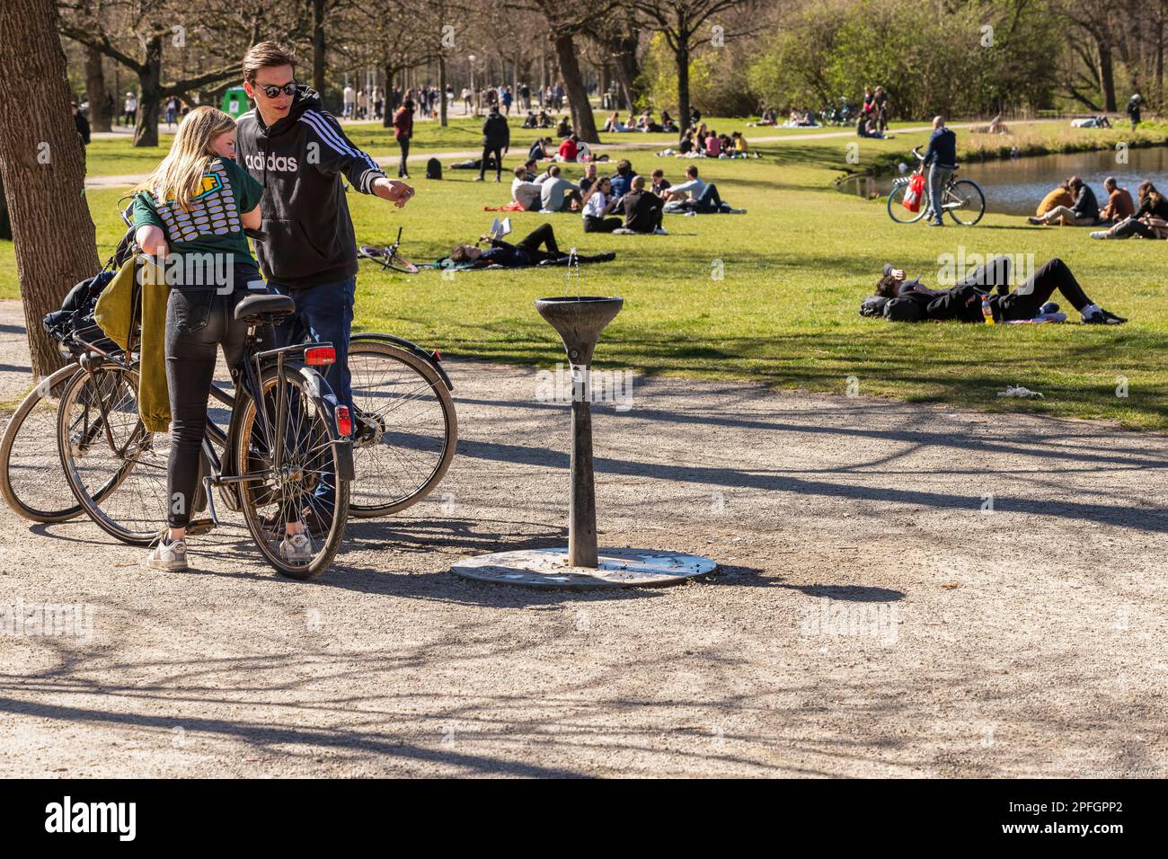 Pointing young people on their bicycles to the green drinking fountain (Dutch: waterhappertje) in the Vondelpark. Stock Photo