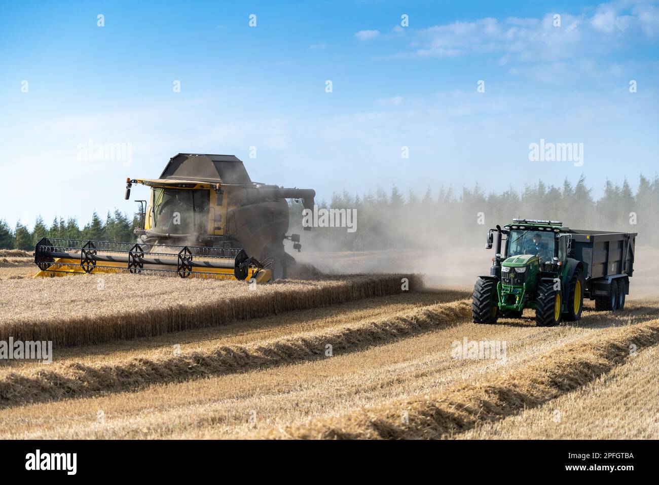 Tractor and trailer driving alongside a combine harvester waiting to pull alongside when needed