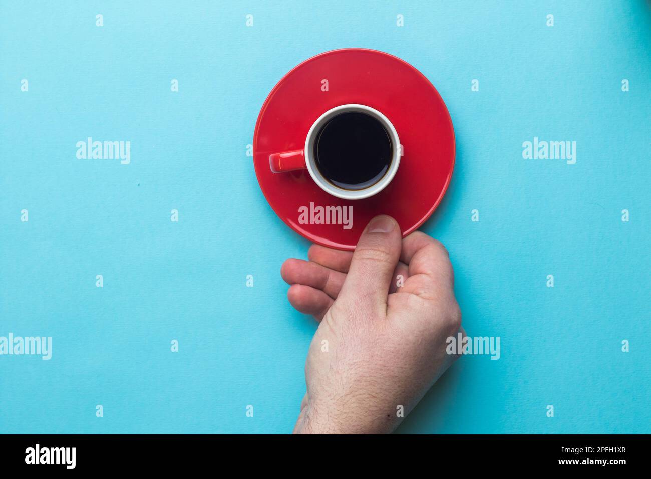 An Espresso cup of black coffee on a saucer being held by a hand on a blue back ground Stock Photo