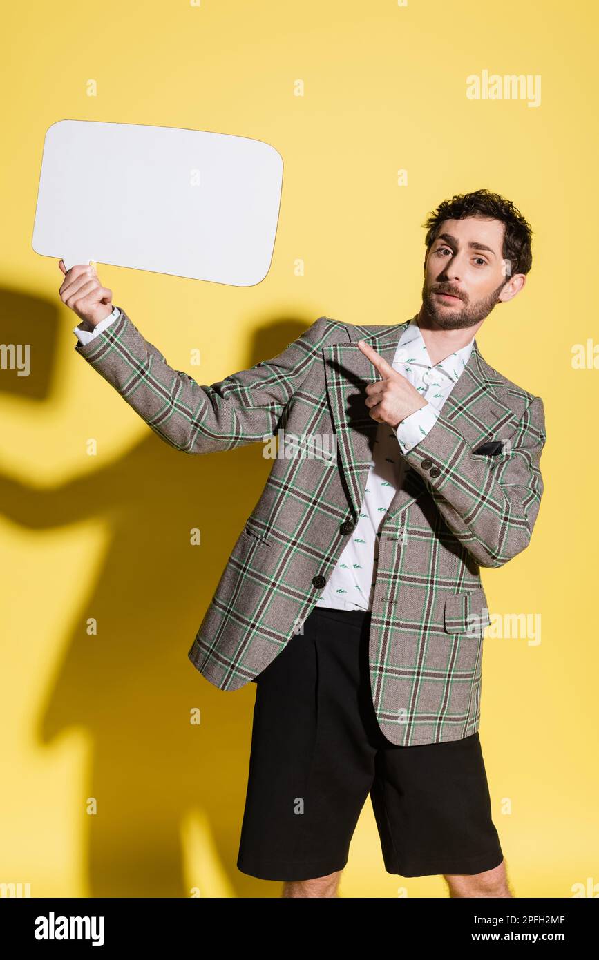 Charming guy in jacket pointing at empty speech bubble on yellow background,stock image Stock Photo