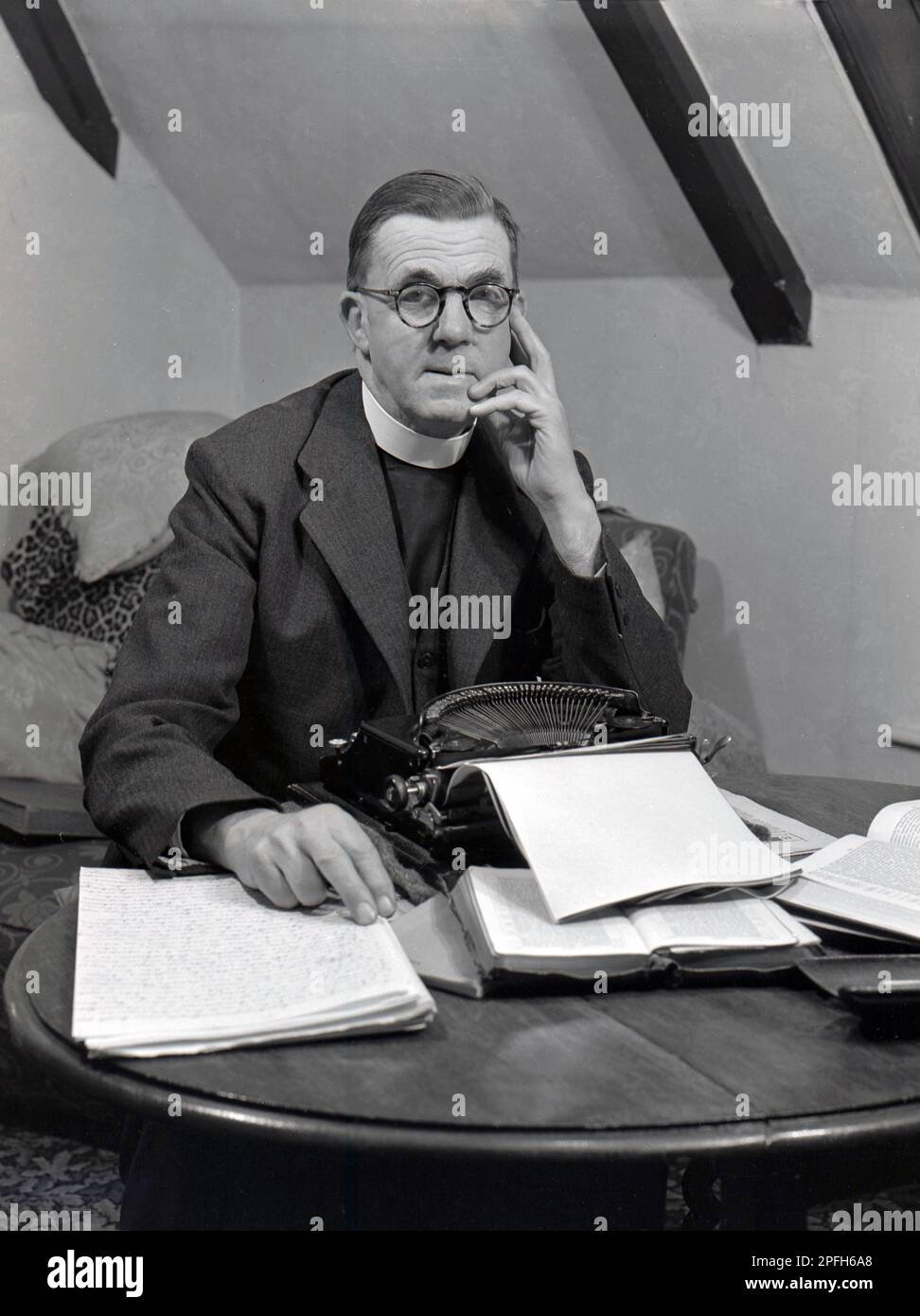 1940s, historial, a vicar, wearing a clerical collar, stting at a desk at a typewriter of the era, with his speech for a service, USA. Stock Photo