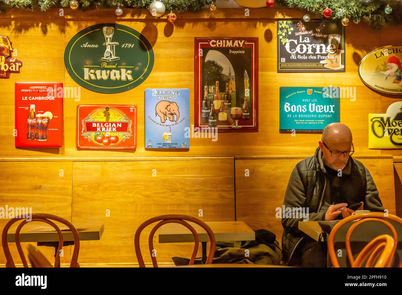 Man sitting in a café in Brussels, consulting his mobile phone in front of a cup of coffee. Advertisements for Belgian beers hang on the wall behind h Stock Photo
