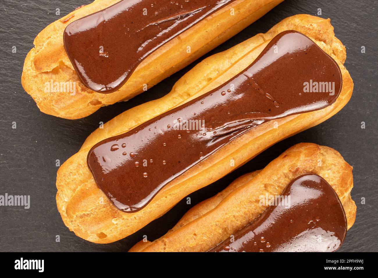 Three chocolate eclairs, close-up, on slate stone, top view. Stock Photo