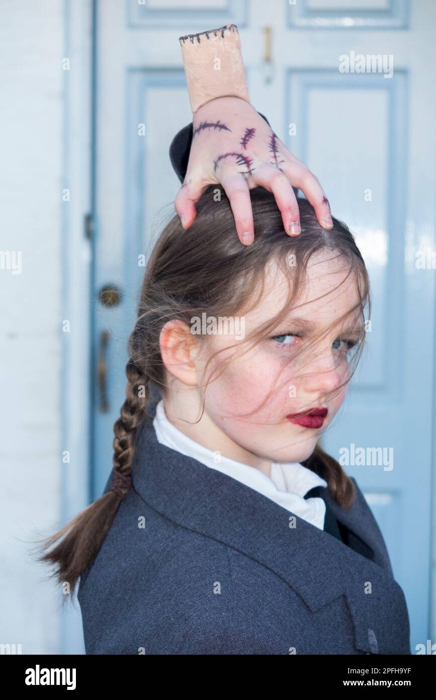 Twelve / 12 year old girl / pupil / child / kid / student goes to school dressed as Wednesday from The Addams Family, with 'Thing', for World Book Day. Stock Photo