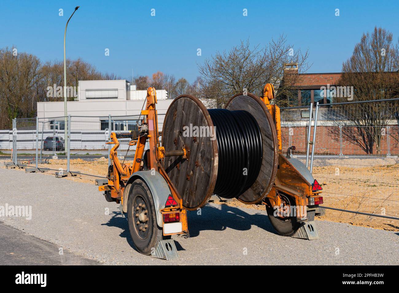 A wooden reel with an electric cable is mounted on a two-wheeled trailer. Construction site. Buildings in the background. Stock Photo