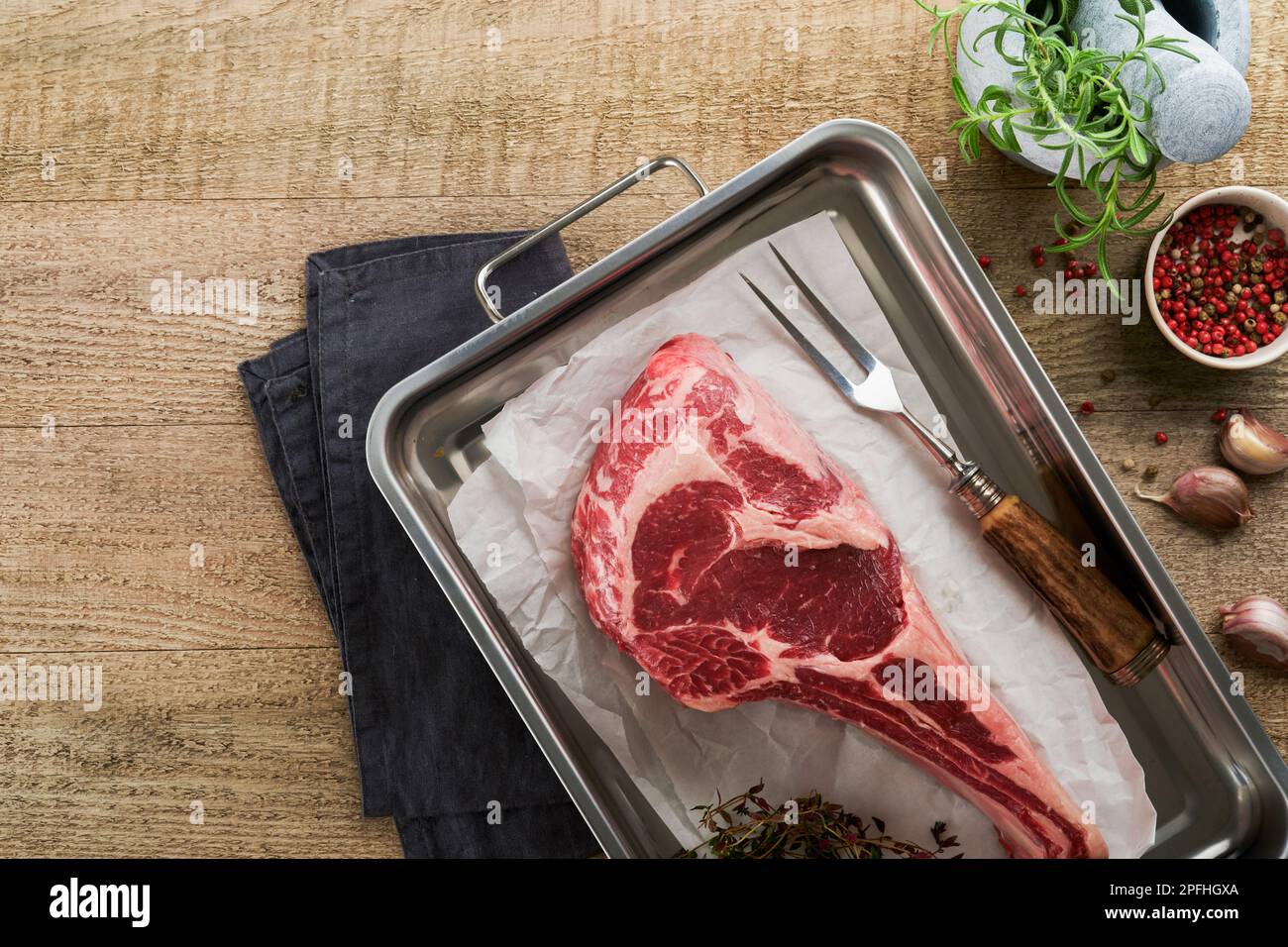 Fresh tomahawk raw steak. Dry aged raw tomahawk beef steak with herbs and salt on old wooden background. Preparing to grill.  Top view and copy space. Stock Photo