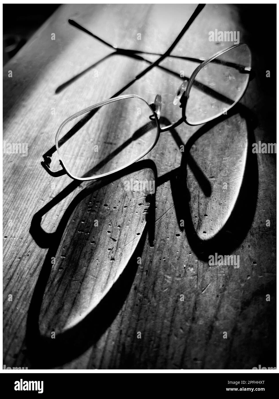 Black and white photo of a pair of eyeglasses with an elongated shadow on a rustic wooden table Stock Photo