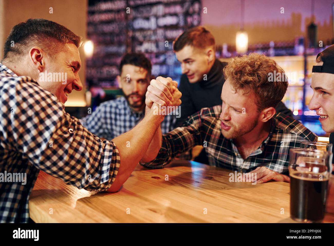 Friends plays arm wrestling. Group of people together indoors in the ...