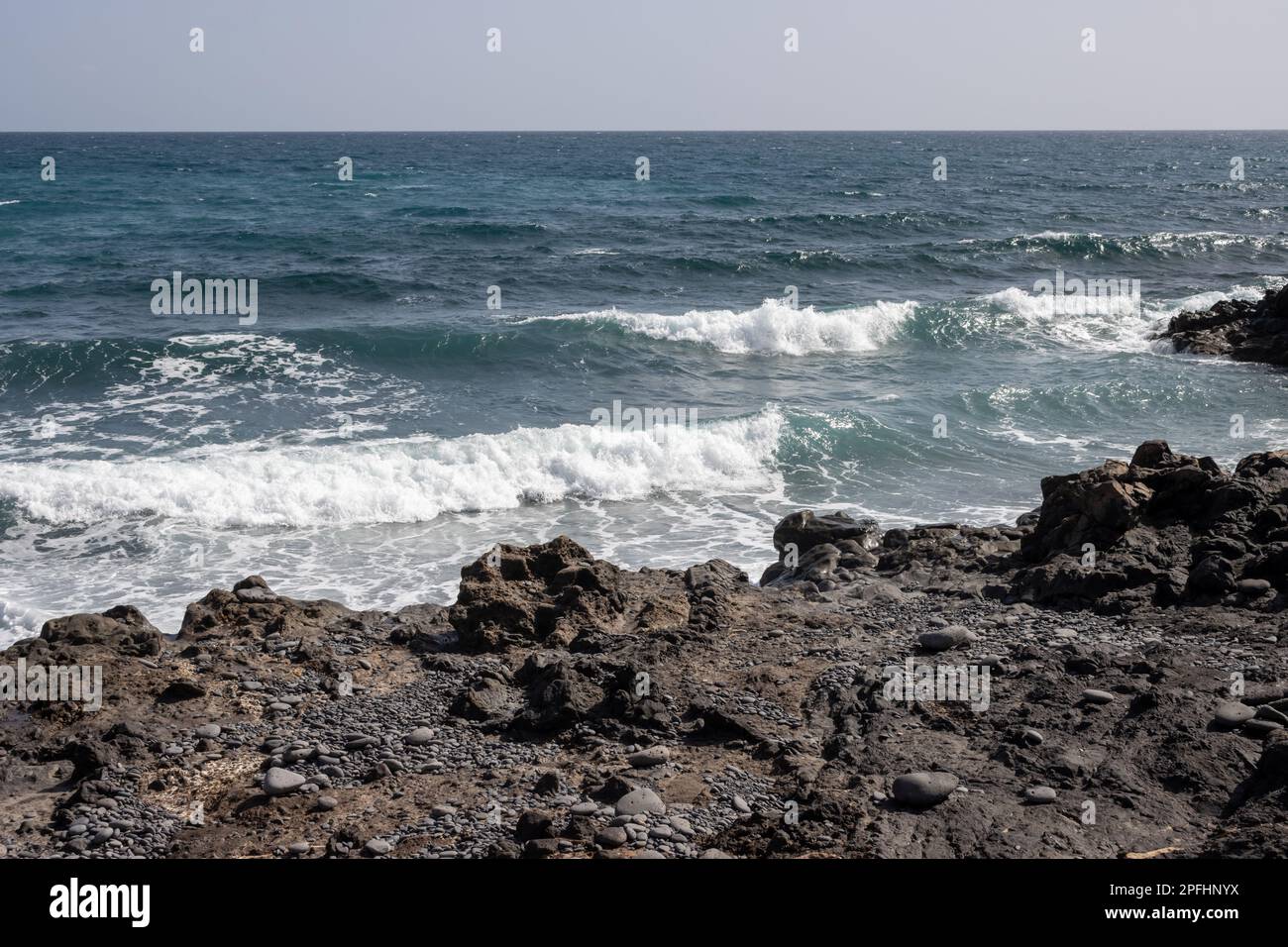 Atlantic ocean with small waves. Black rocks at the coast. Blue sky on a horizon. Fabrica de callao de los Pozos, Puerto del Rosario, Fuerteventura, S Stock Photo