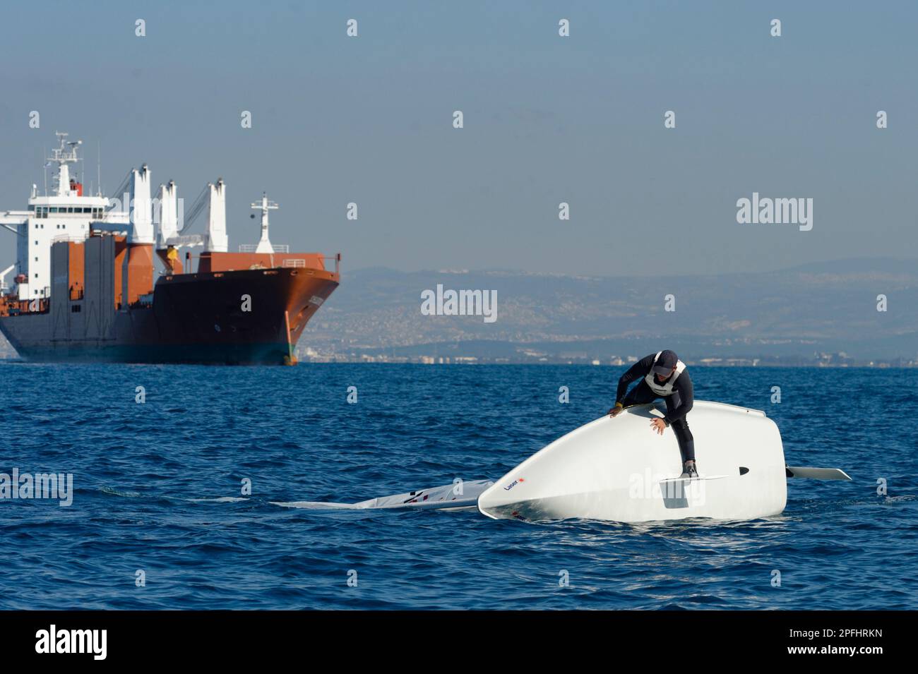 Photo of a sailor astride the capsized laser class sailboat with a