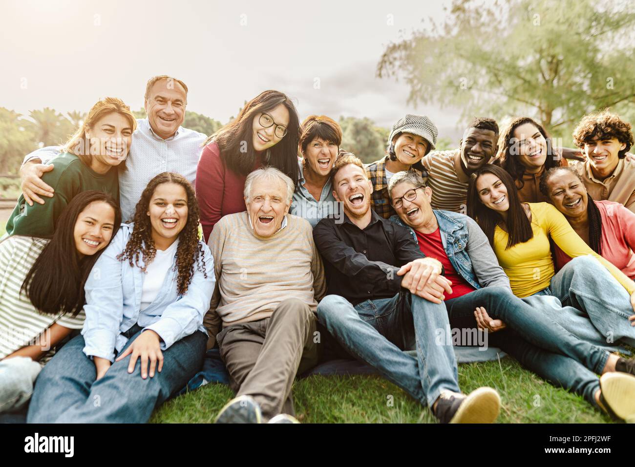 Happy multigenerational people having fun sitting on grass in a public park Stock Photo