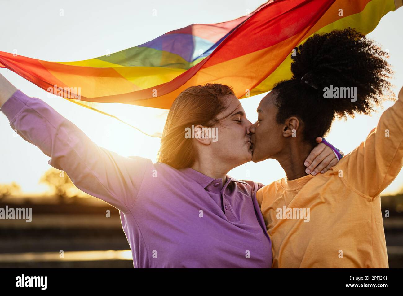 Lesbian couple kissing while holding rainbow flag during gay pride celebration outdoor - Lgbt and love equality concept Stock Photo