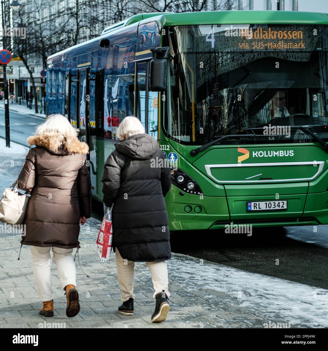 Stavanger, Norway, March 10 2023, Two Middle Aged Women Walking Past A Green Kolumbus Single Deck Bus Stock Photo