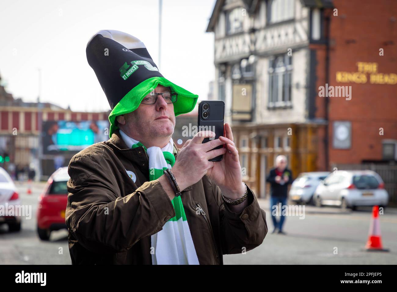 2023 St Patrick’s Day Parade in Warrington. Man in Guinness hat takes photo on his phone Stock Photo