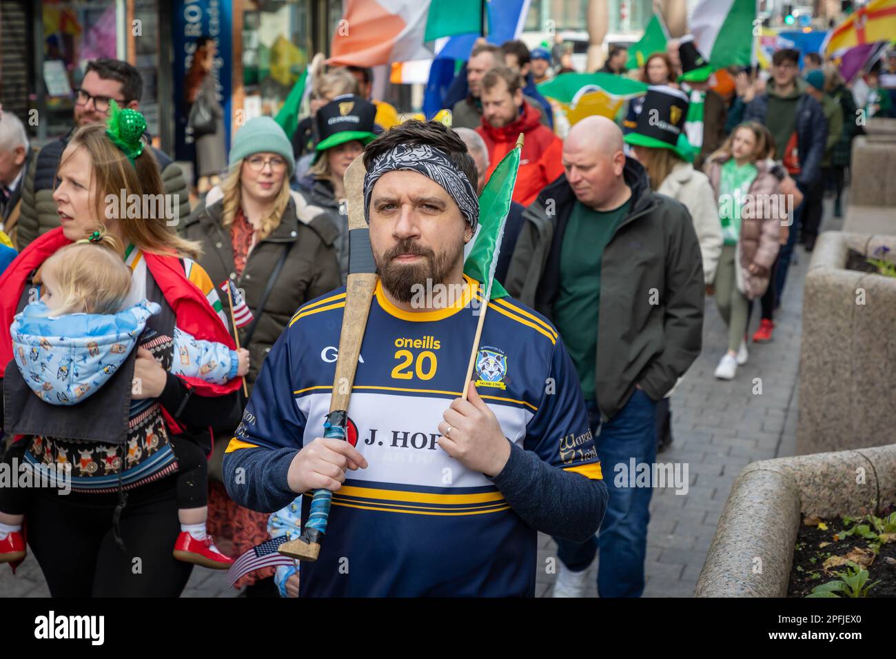 2023 St Patrick’s Day Parade in Warrington. Local hurling player with Hurley and Bandana joins the public Stock Photo