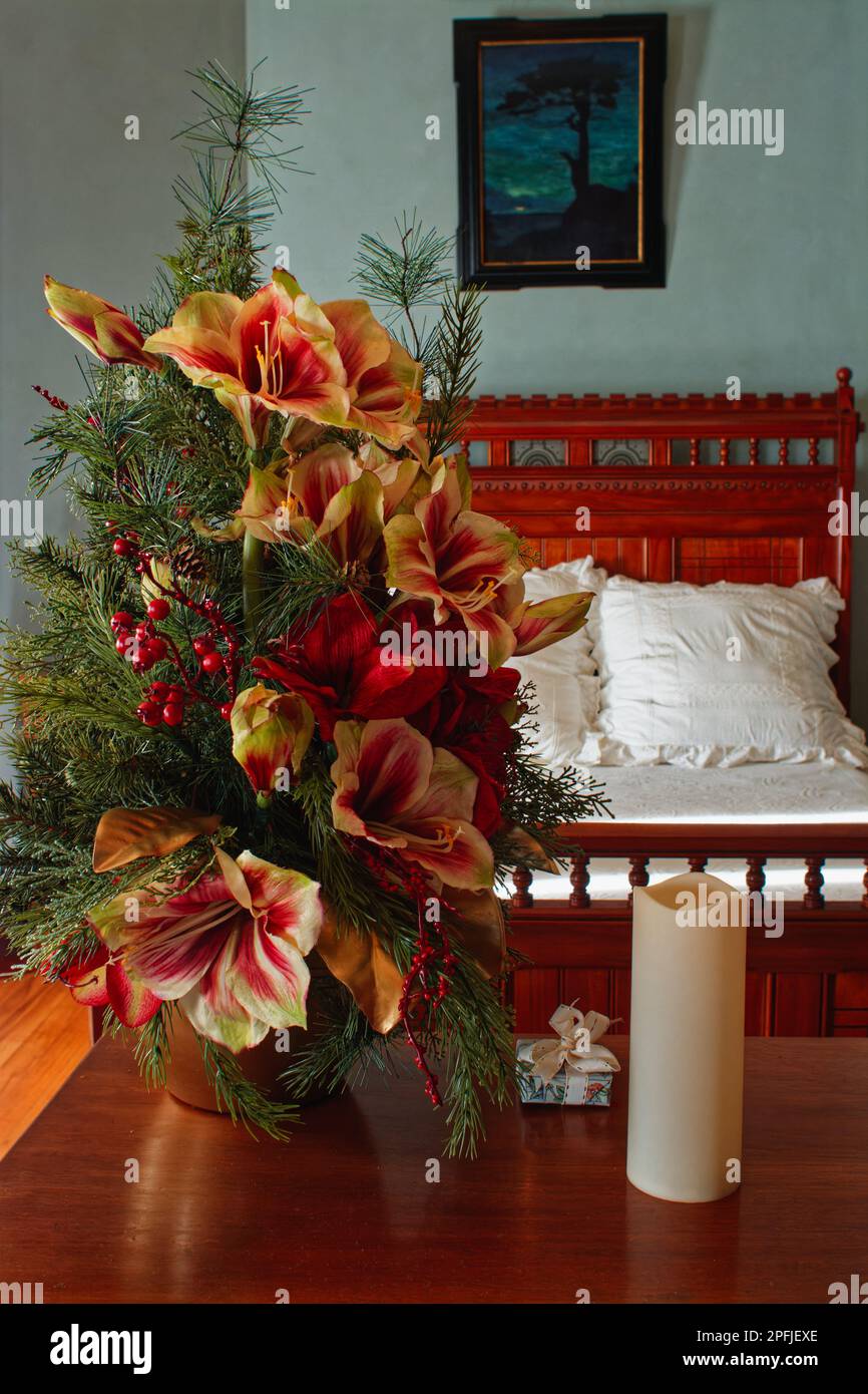 A colorful Christmas flower arrangement and small gift are displayed on a bedroom table with a bed covered in white linen in the background at the 187 Stock Photo