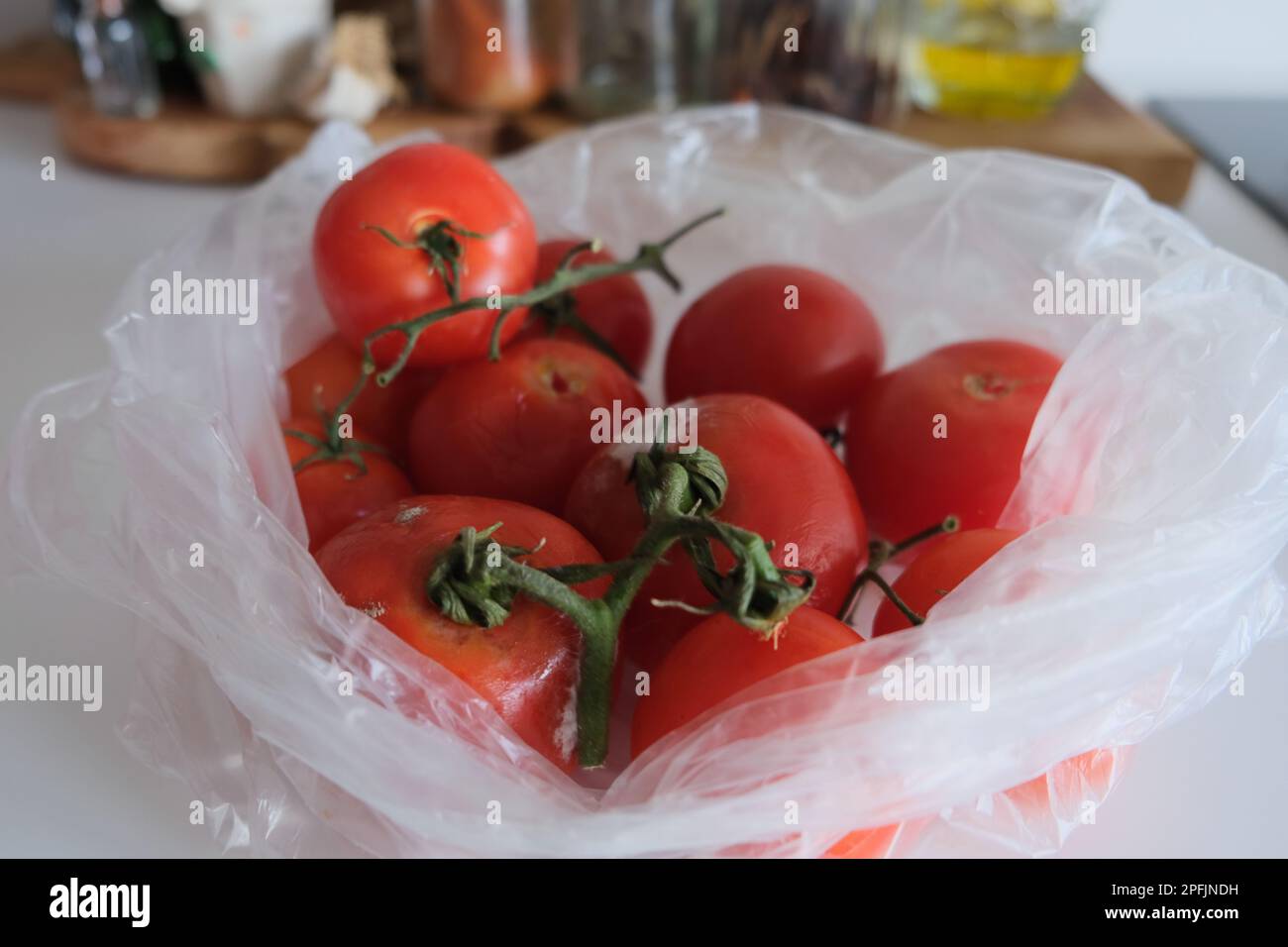 Some rotten tomatoes and some pristine tomatoes are in a transparent plastic bag on a white kitchen countertops. Stock Photo