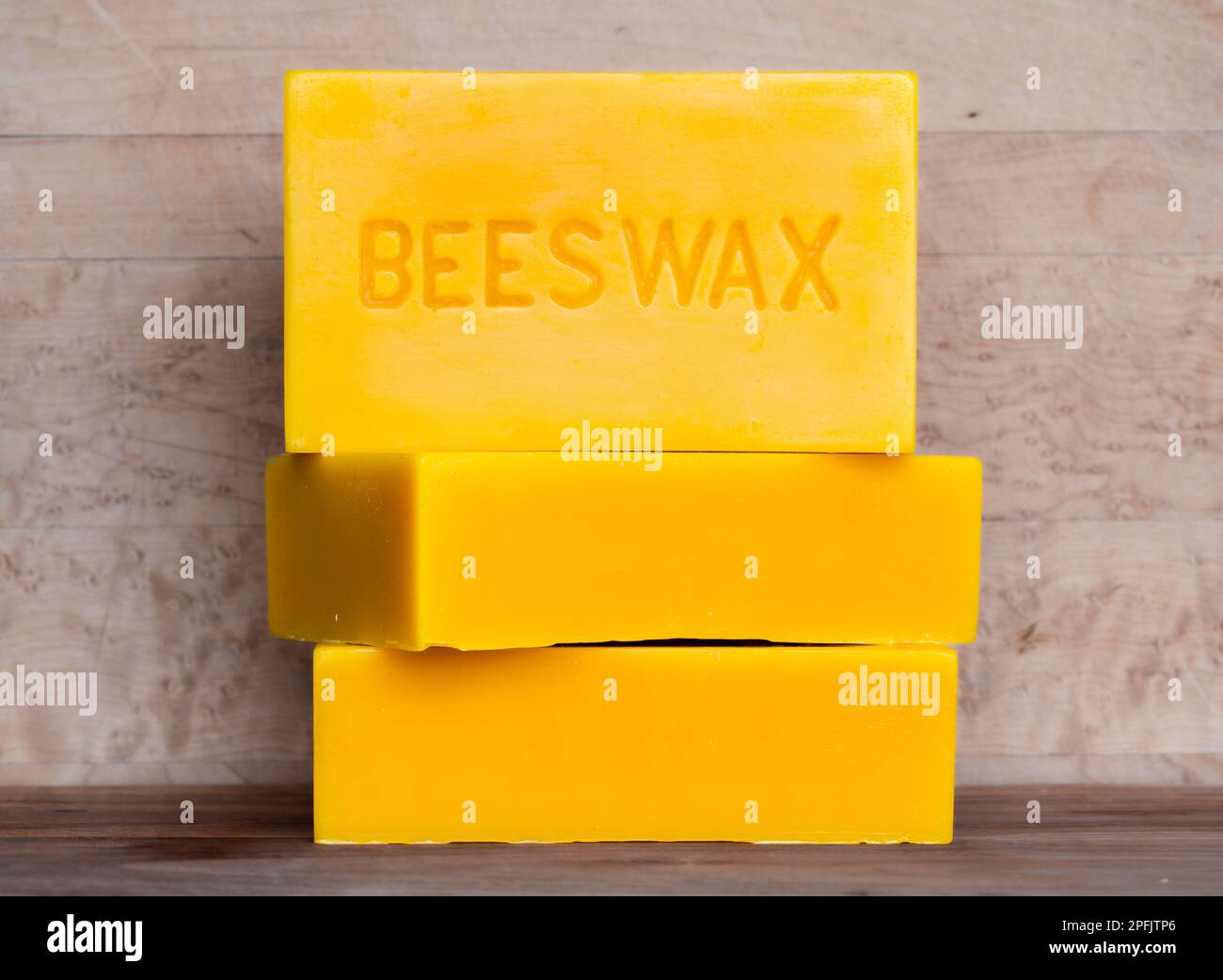 Three bricks of pure bees wax stacked against a wood background Stock Photo