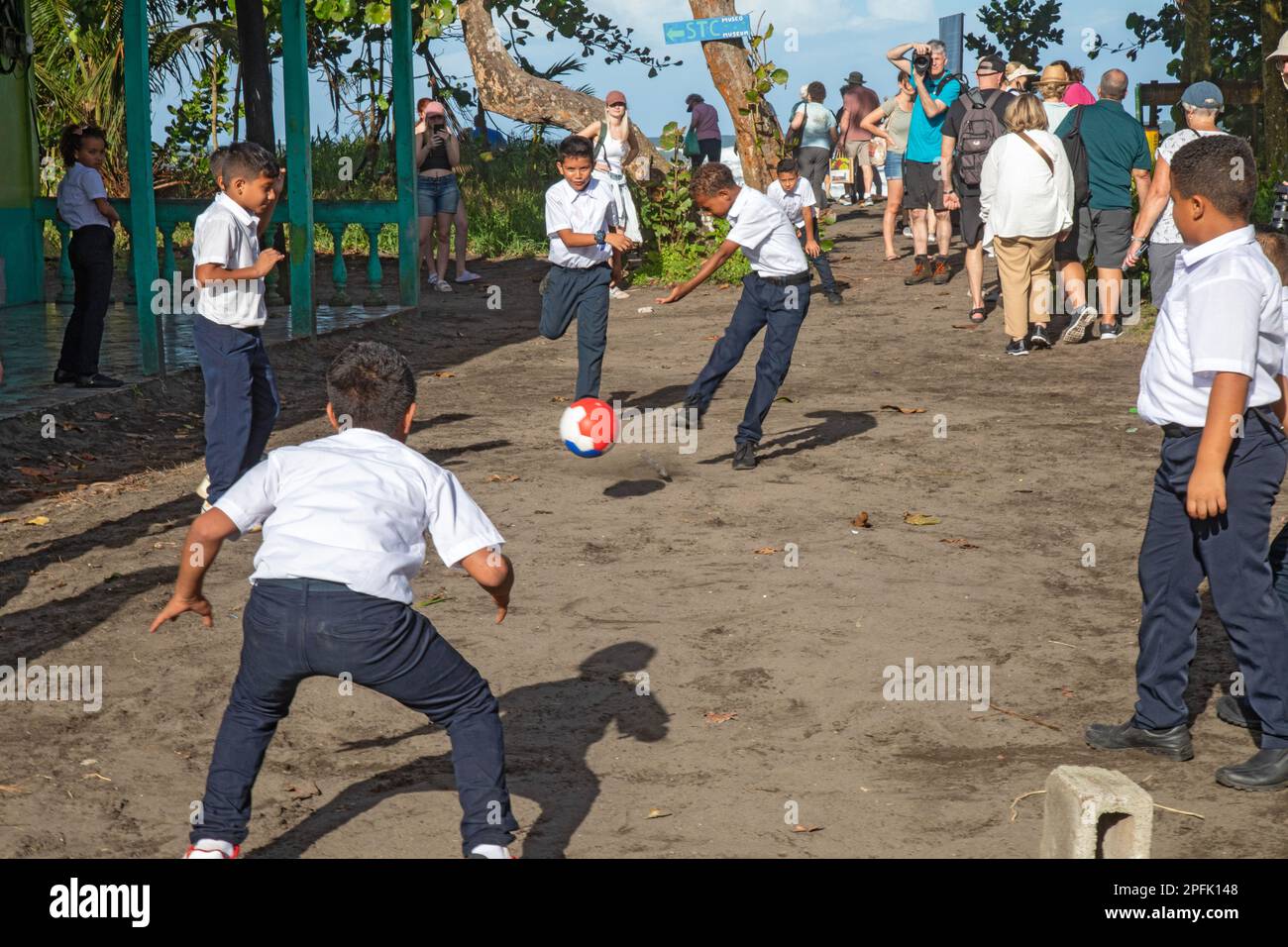 Tortuguero, Costa Rica - As tourists walk by, school boys play football (soccer) outside their school in this small village on the Caribbean coast. Co Stock Photo