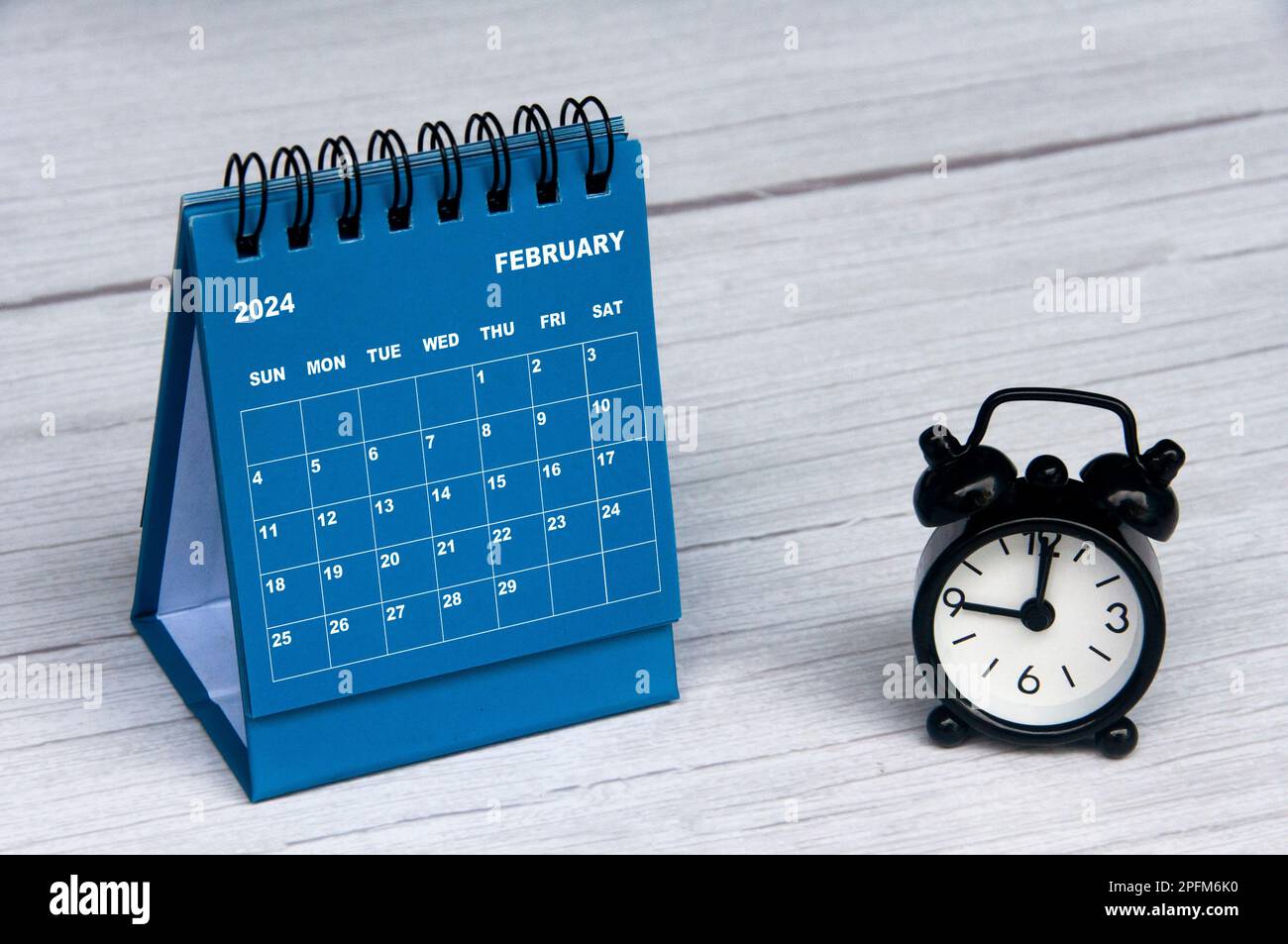 February 2024 calendar on wooden desk and alarm clock with customizable space for text. Monthly