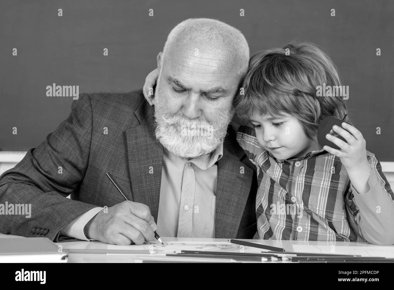 Pupil in class draw with teacher. Educational process. Thank You Teacher. Portrait of senior teacher and little boy kid sitting at desk in classroom. Stock Photo