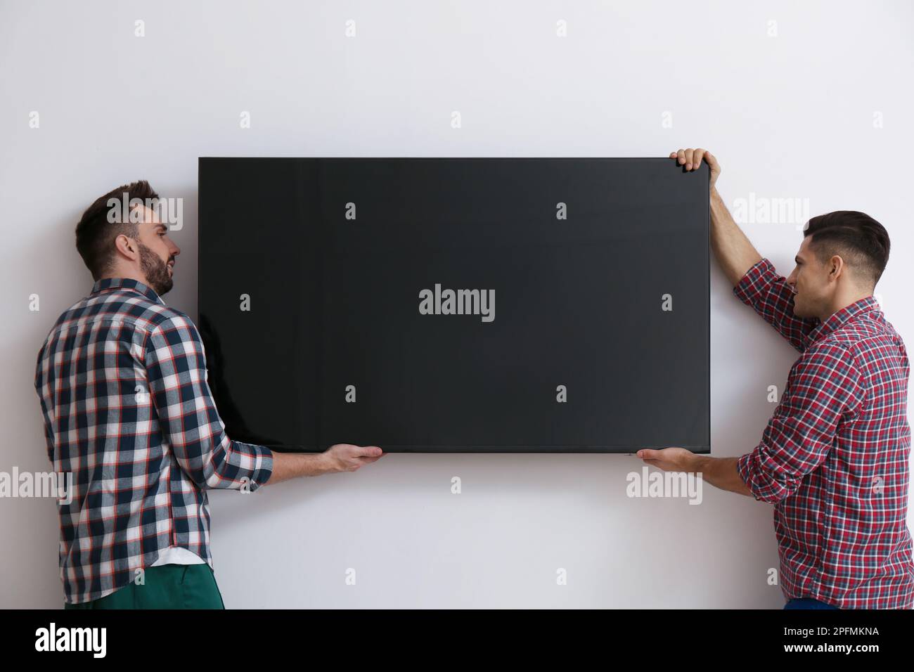 Men installing modern flat screen TV on wall indoors Stock Photo