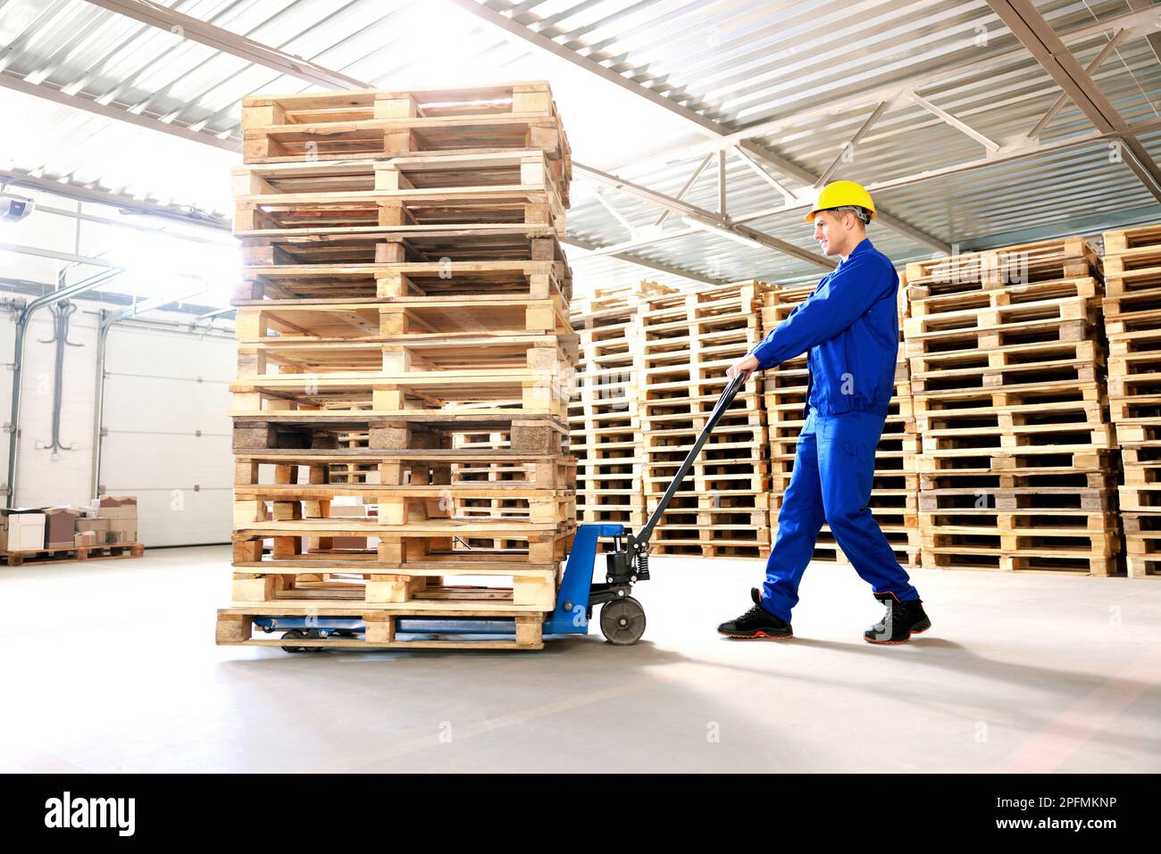 Worker moving wooden pallets with manual forklift in warehouse Stock ...