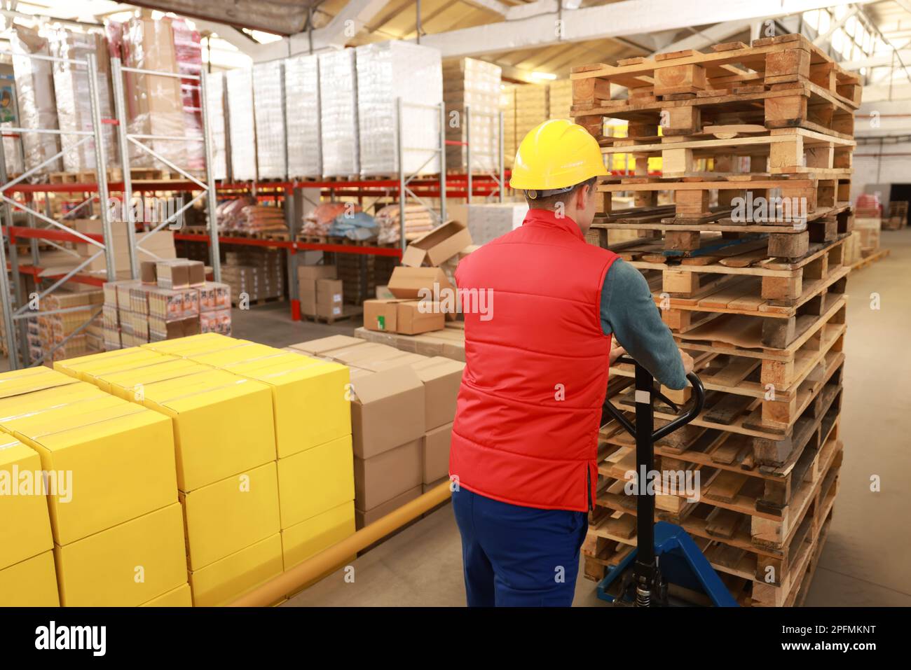 Worker moving wooden pallets with manual forklift in warehouse, back ...