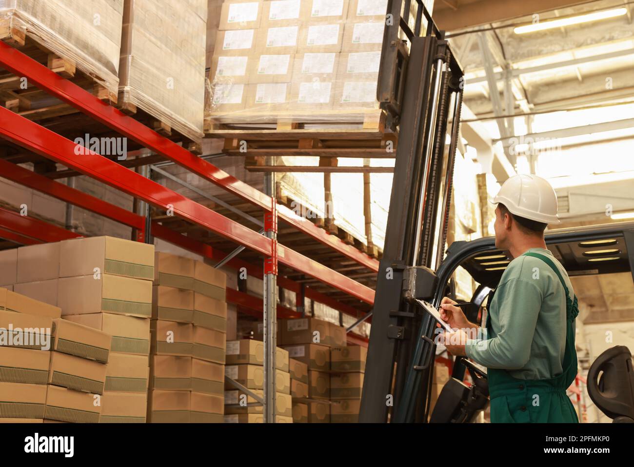Worker near forklift truck with cardboard boxes in warehouse. Logistics ...