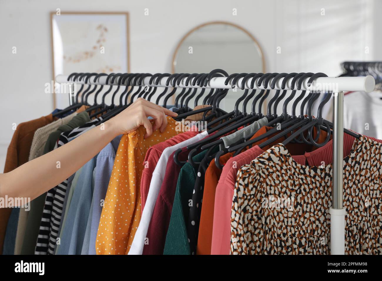 Woman picking clothes from rack indoors, closeup. Fast fashion Stock