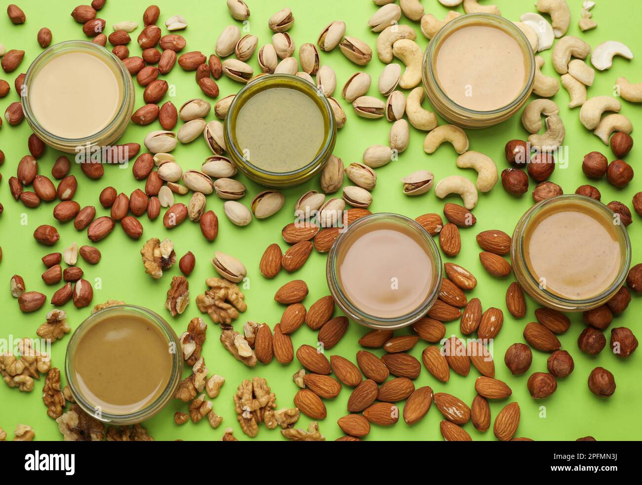 Different types of delicious nut butters and ingredients on light green