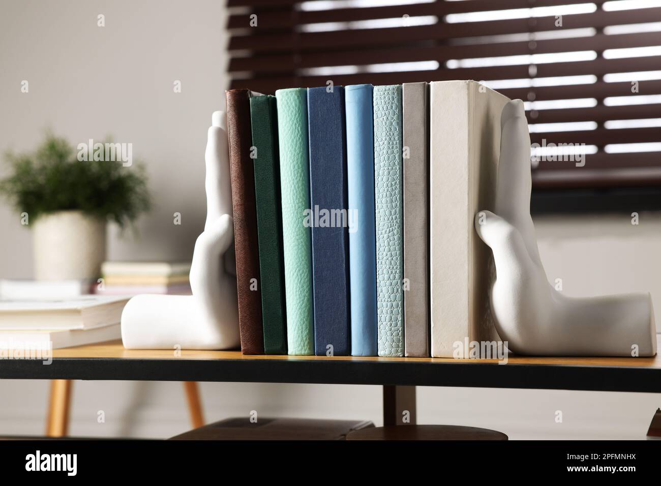 Beautiful hand shaped bookends with books on shelf indoors Stock Photo