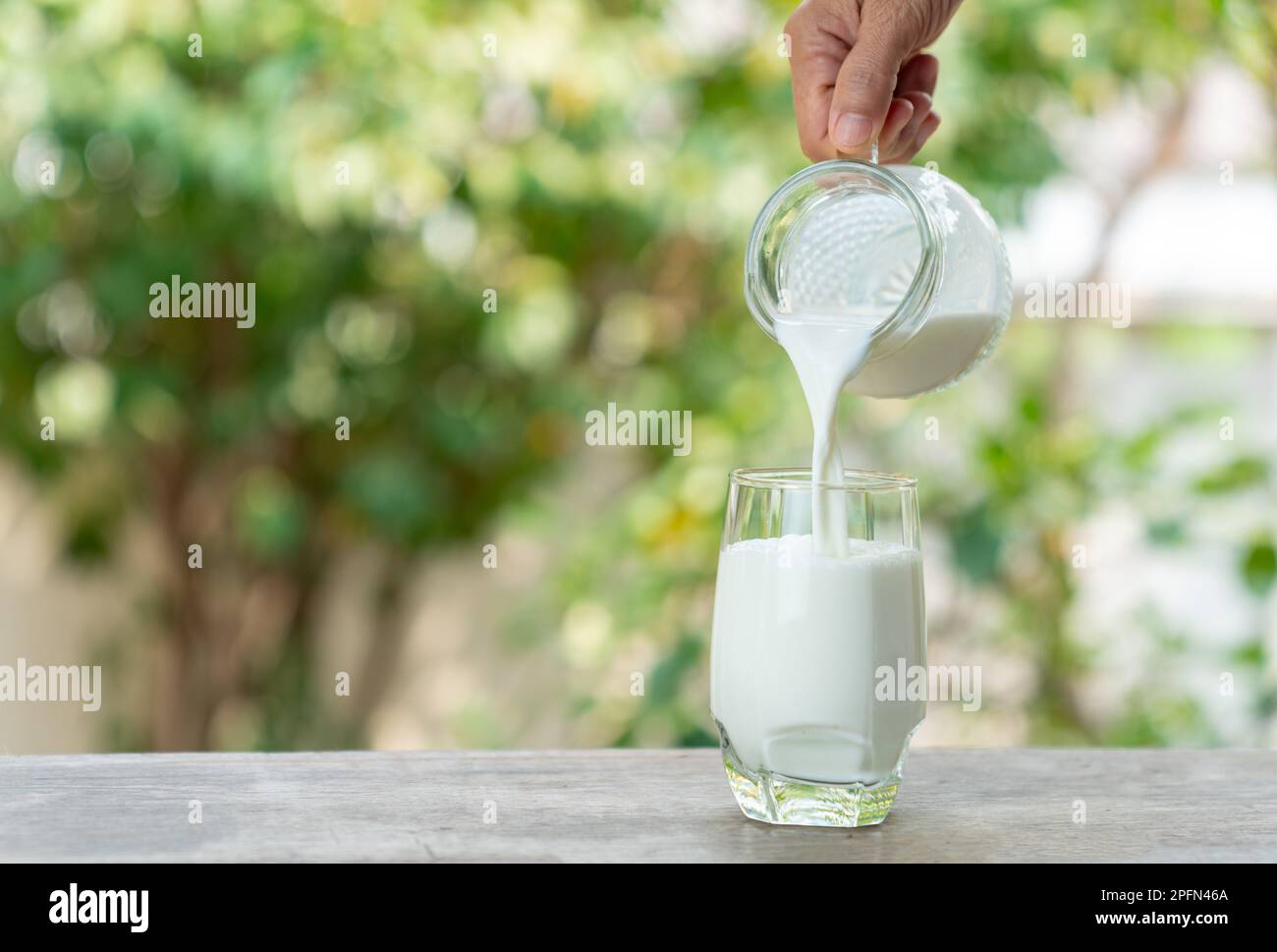 Close up hand hold jug milk pouring into glass on out of focus