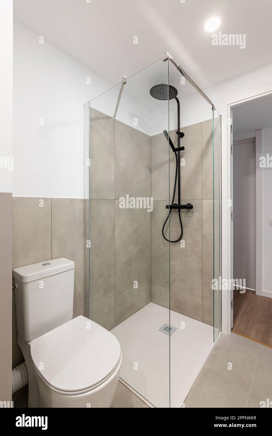 An empty tiny bathroom with a toilet and a glazed shower with gray ...