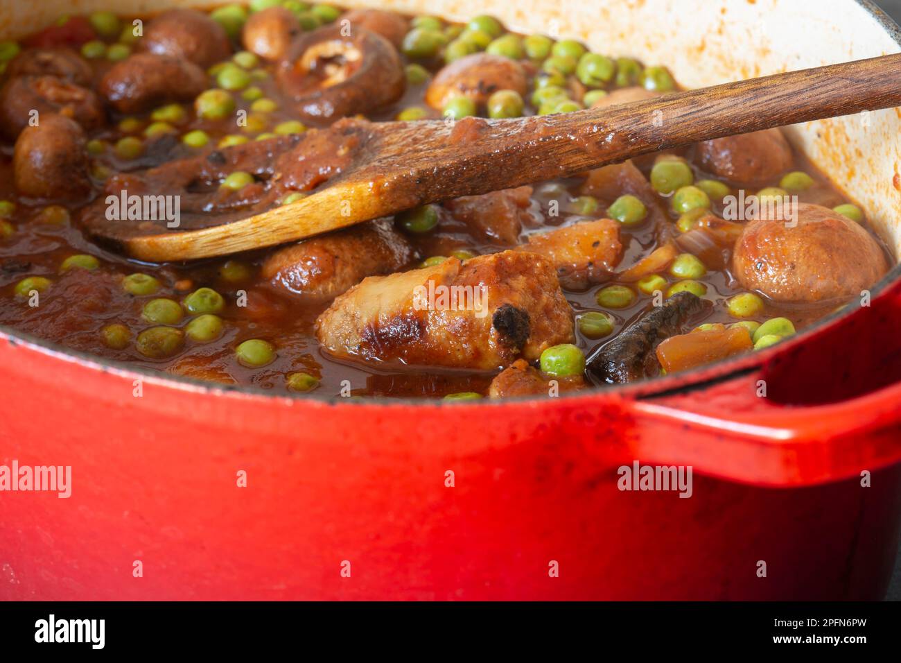 Sausage casserole in a red casserole dish, with potato, mushrooms