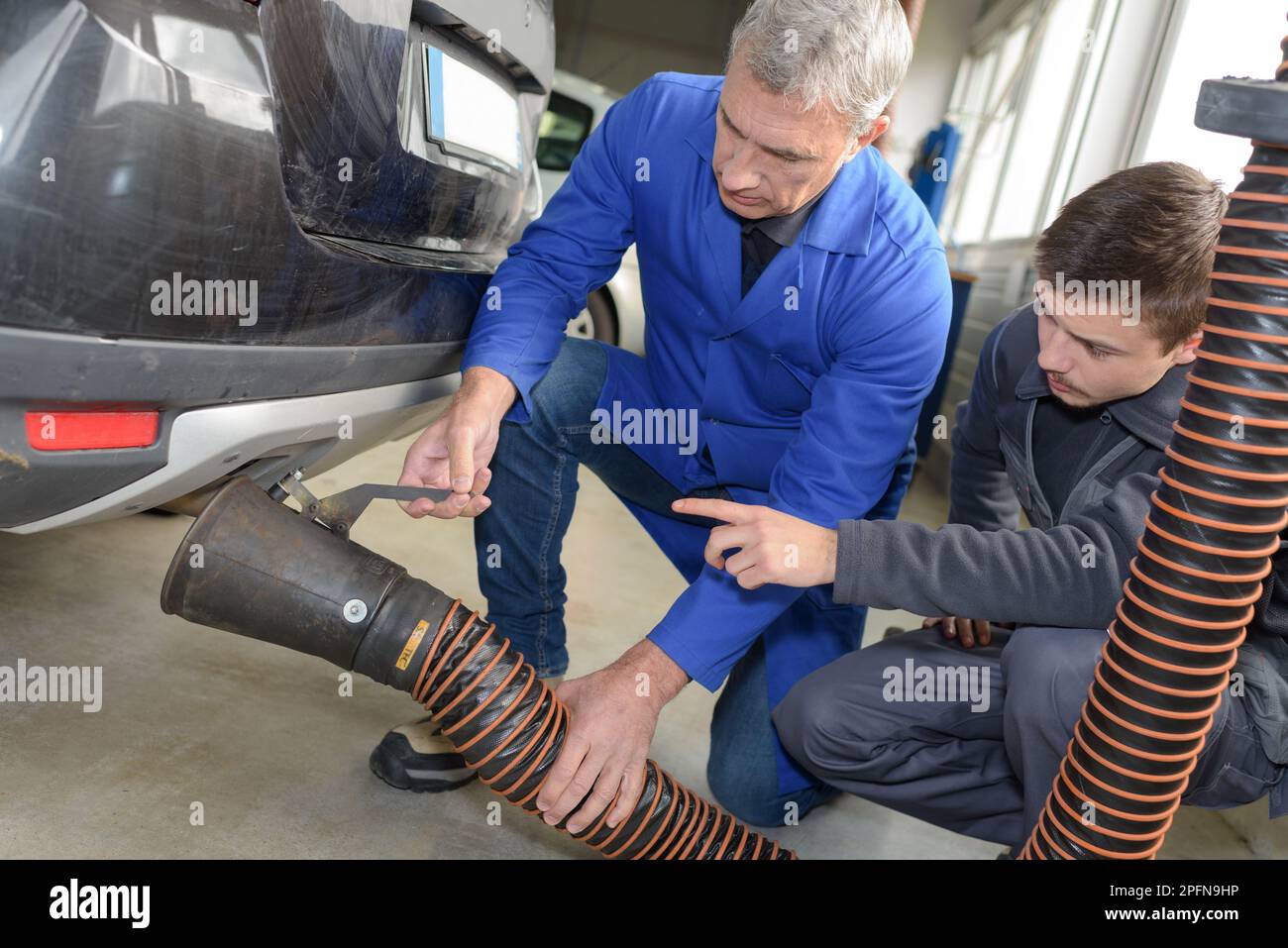 professional trainer teaching student how to fix car exhaust pipe Stock