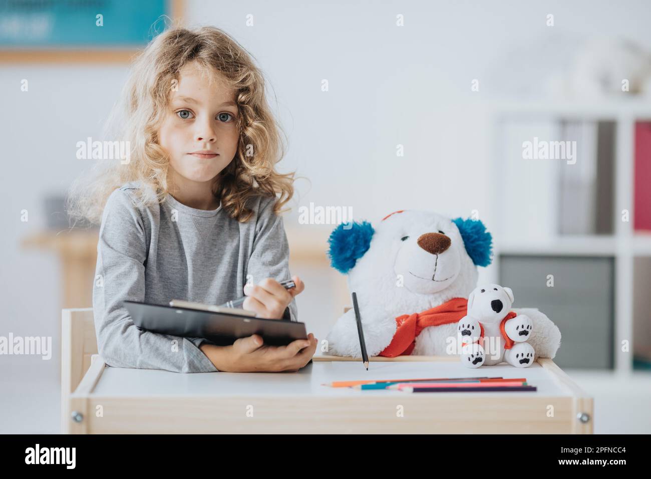 Young autistic boy sitting with a teddy bear by a school desk Stock