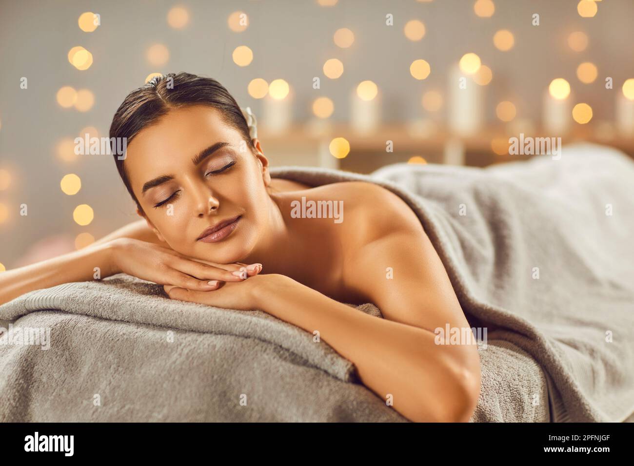 Young woman lying with closed eyes alone on massage couch in salon at wellness center Stock Photo