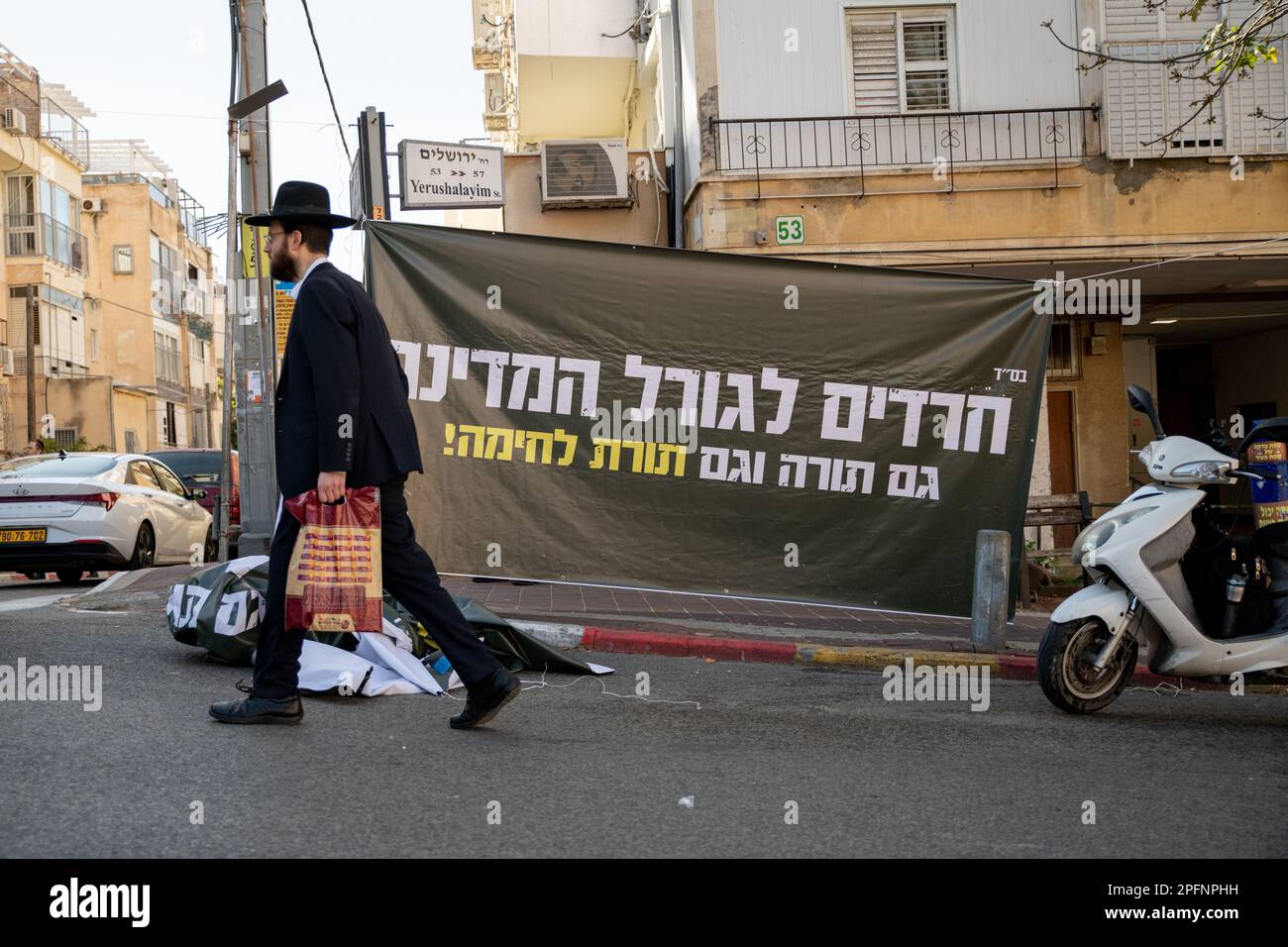 Israel. 16th Mar, 2023. An orthodox man passes next to a protest against the reform sign that reads “Haredim/anxious for the fate of the country, Torah as well as martial theory/Torah”. Israeli reserve soldiers against the reform open a “recruiting centre” to IDF military service in a protestation act in the Ultra-Orthodox city of Bnei Brak. Bnei Brak, Israel. Mar 16th 2023. (Photo by Matan Golan/Sipa USA). Credit: Sipa USA/Alamy Live News Stock Photo