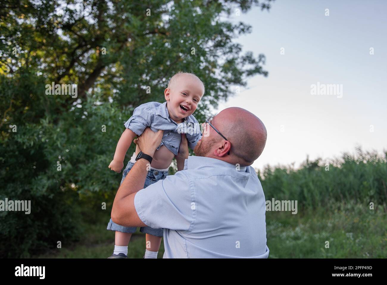 Bald man with glasses throws child into the sky air. Father in jeans